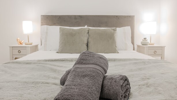 Ein ordentlich bezogenes Bett mit grauer Decke und Kissen, zwei Nachttische mit Lampen und ein Kopfteil.
