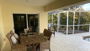A patio with a dining table, chairs, and a grill. - The Island House on Pine Island
with heat-pump heated  most privacy pool (Bokeelia)