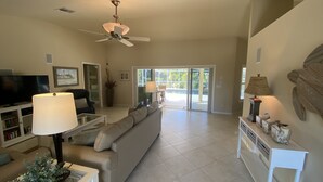 A spacious living room with a ceiling fan, a television, a sofa, a coffee table, and a lamp. - The Island House on Pine Island
with heat-pump heated  most privacy pool (Bokeelia)