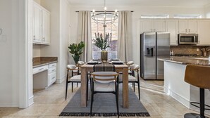 A modern kitchen with white cabinets, stainless steel appliances, and a dining area with a wooden table and chairs. - Spacious 4BR/4.5BA, Pool & Heated Spa, Close Proximity to Dining, Shopping & Fun (Plano)