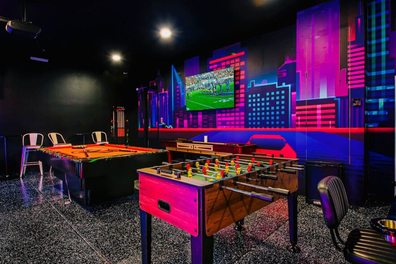 A room with a foosball table, a pool table, and a projection screen displaying a sports game.