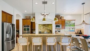 Une cuisine moderne dotée d’appareils électroménagers en acier inoxydable, de meubles en bois, d’un grand îlot central avec des tabourets de bar et d’un éclairage suspendu.