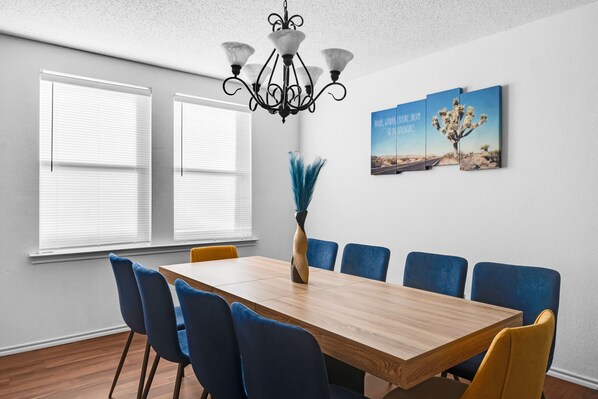 Une salle de conférence avec une table en bois, des chaises bleues et jaunes, un lustre et un tableau représentant un paysage désertique accroché au mur.