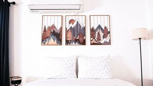 A hotel room with a bed, a wall-mounted air conditioner, and three framed artworks depicting mountains and trees. - Yosemite's Natures Tranquility Cottage (Ahwahnee)