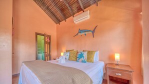 Ein Schlafzimmer mit Bett, Kissen, einem Nachttisch, einer Wand-Klimaanlage und einer Tür.