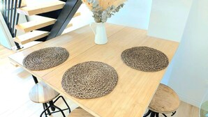 Ein Essbereich mit einem Holztisch, vier gewebten Platzsets, zwei Stühlen und einer Vase mit Trockenblumen.
