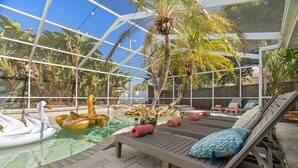 A glass-enclosed pool area with lounge chairs and swan and duck inflatable toys.