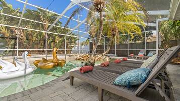 A glass-enclosed pool area with lounge chairs and swan and duck inflatable toys.