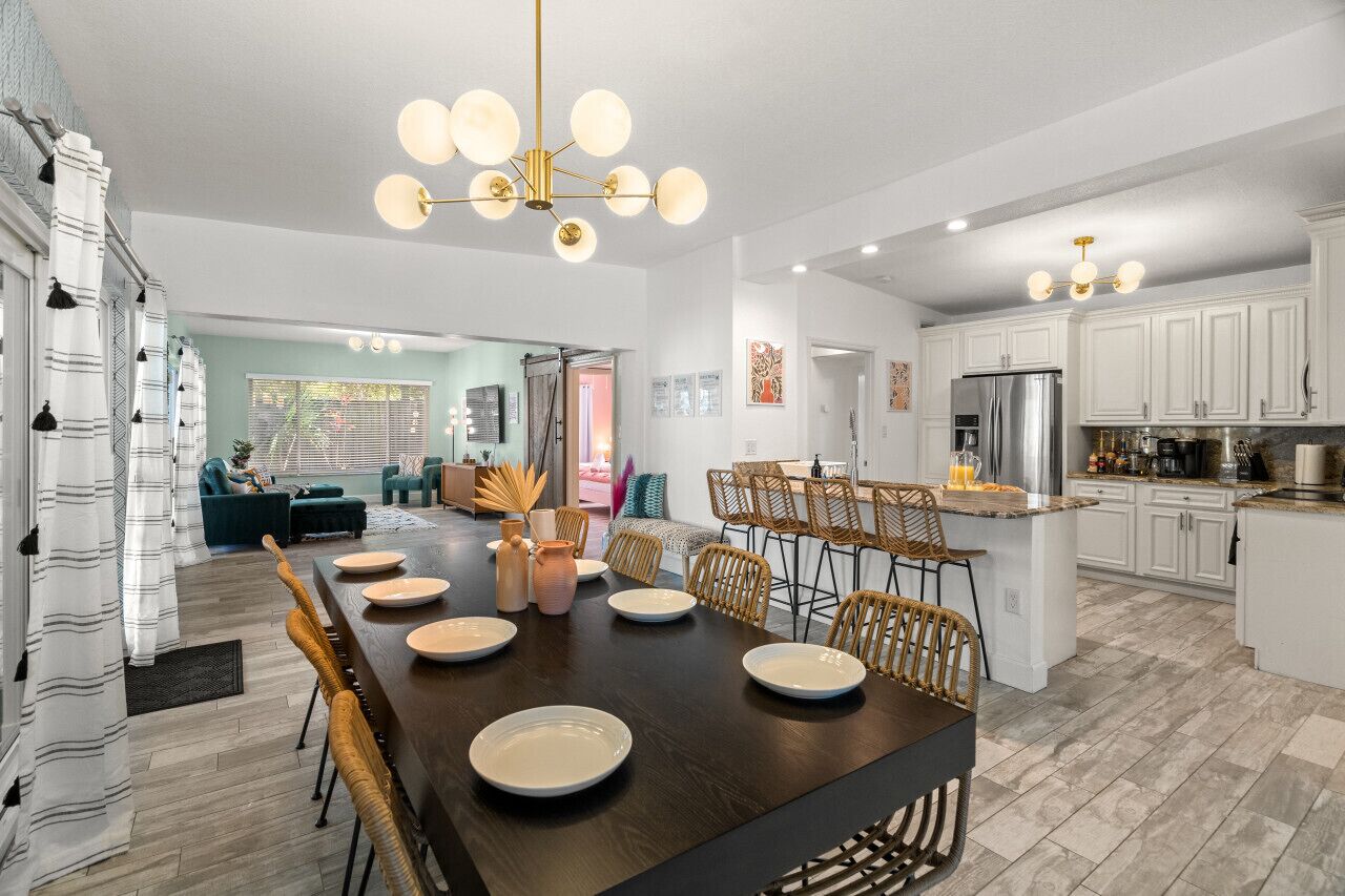A modern kitchen with white cabinets, a central island, and a dining area with a dark wood table and chairs.