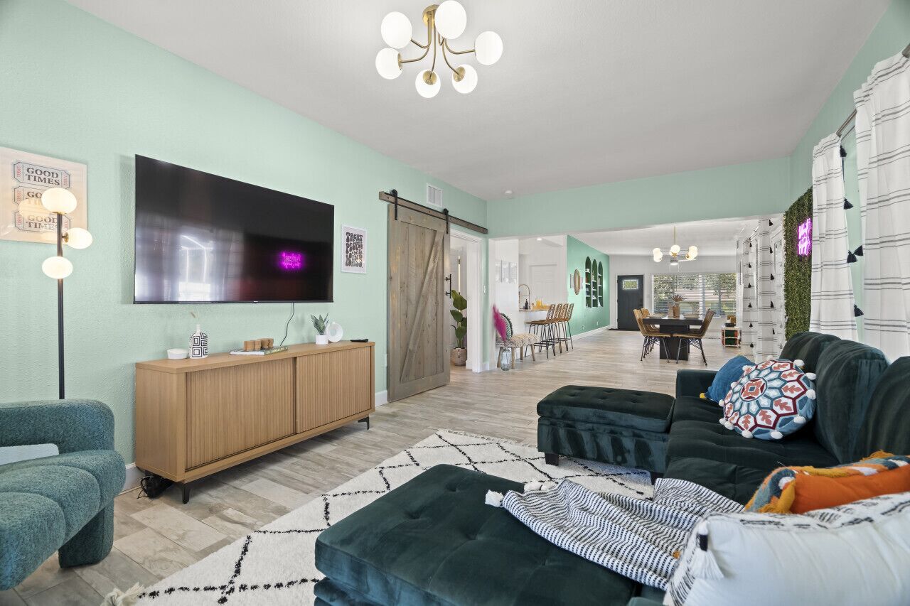 Un salon moderne avec un grand téléviseur à écran plat, un meuble en bois, un canapé foncé et un tapis à motifs.