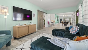 A modern living room with a large flat-screen TV, a wooden cabinet, a dark sofa, and a patterned rug.