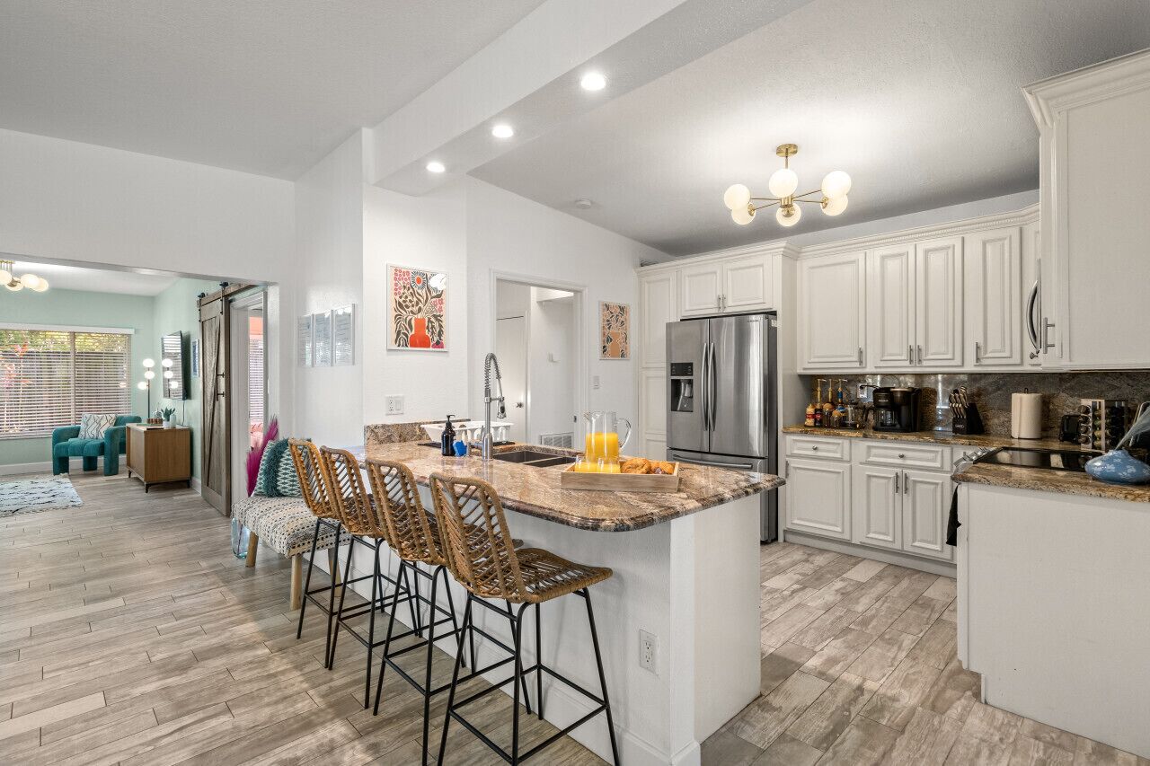 A spacious kitchen with white cabinets, a large island with bar stools, stainless steel appliances, and a wooden floor.