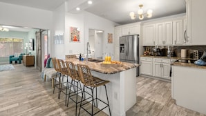 A spacious kitchen with white cabinets, a large island with bar stools, stainless steel appliances, and a wooden floor.