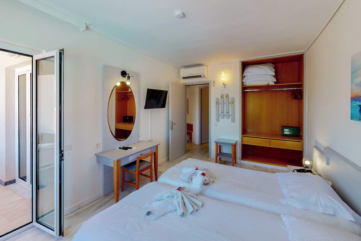 A hotel room with a bed, a desk, a mirror, a wardrobe, and a TV.