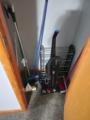 A narrow hallway with a vacuum cleaner, a broom, and a mop leaning against the wall.