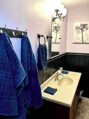 A bathroom with a black bathtub, a beige sink, and a mirror. There are towels hanging on hooks and a towel rack.