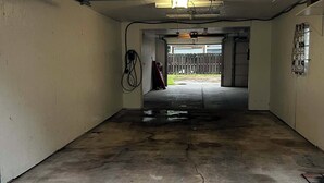 Eine Garage mit Betonboden, einem roten Gegenstand im Hintergrund und einer an der Wand montierten Leuchte.