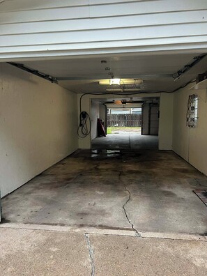 Eine Garage mit Betonboden, einem roten Gegenstand im Hintergrund und einer an der Wand montierten Leuchte.