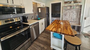 Una cocina moderna con electrodomésticos de acero inoxidable, una mesa de comedor de madera y vista a la playa a través de la puerta abierta.