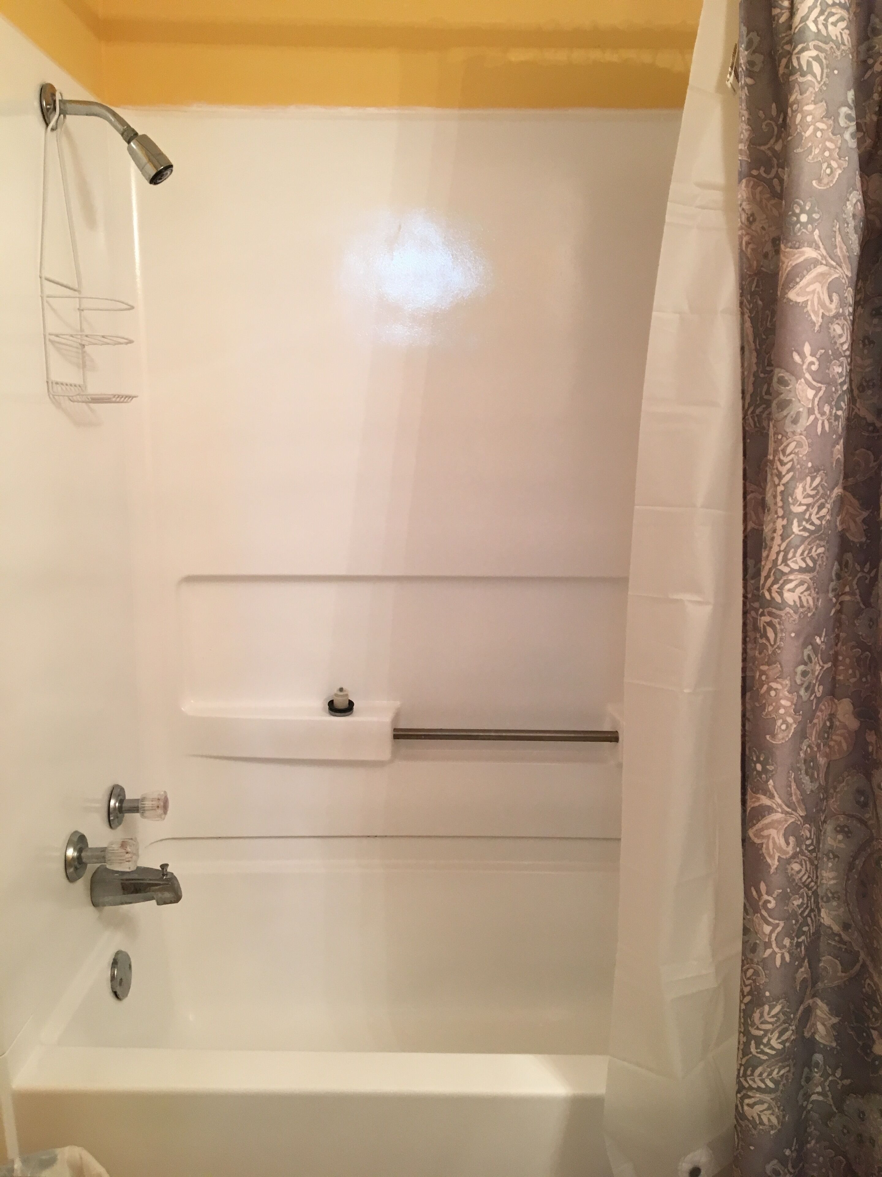 A white bathtub with a showerhead, a towel rack, and a shelf.