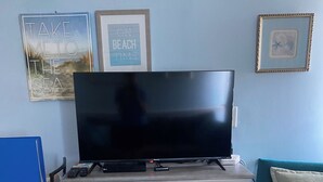 Una sala de estar con una televisión de pantalla plana sobre un mueble blanco, un sofá color aguamarina y una pequeña mesa con sillas.