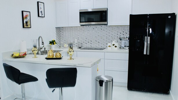 A modern kitchen with white cabinets, a black refrigerator, a microwave, and two bar stools. - Luxury studio near IAH (Humble)