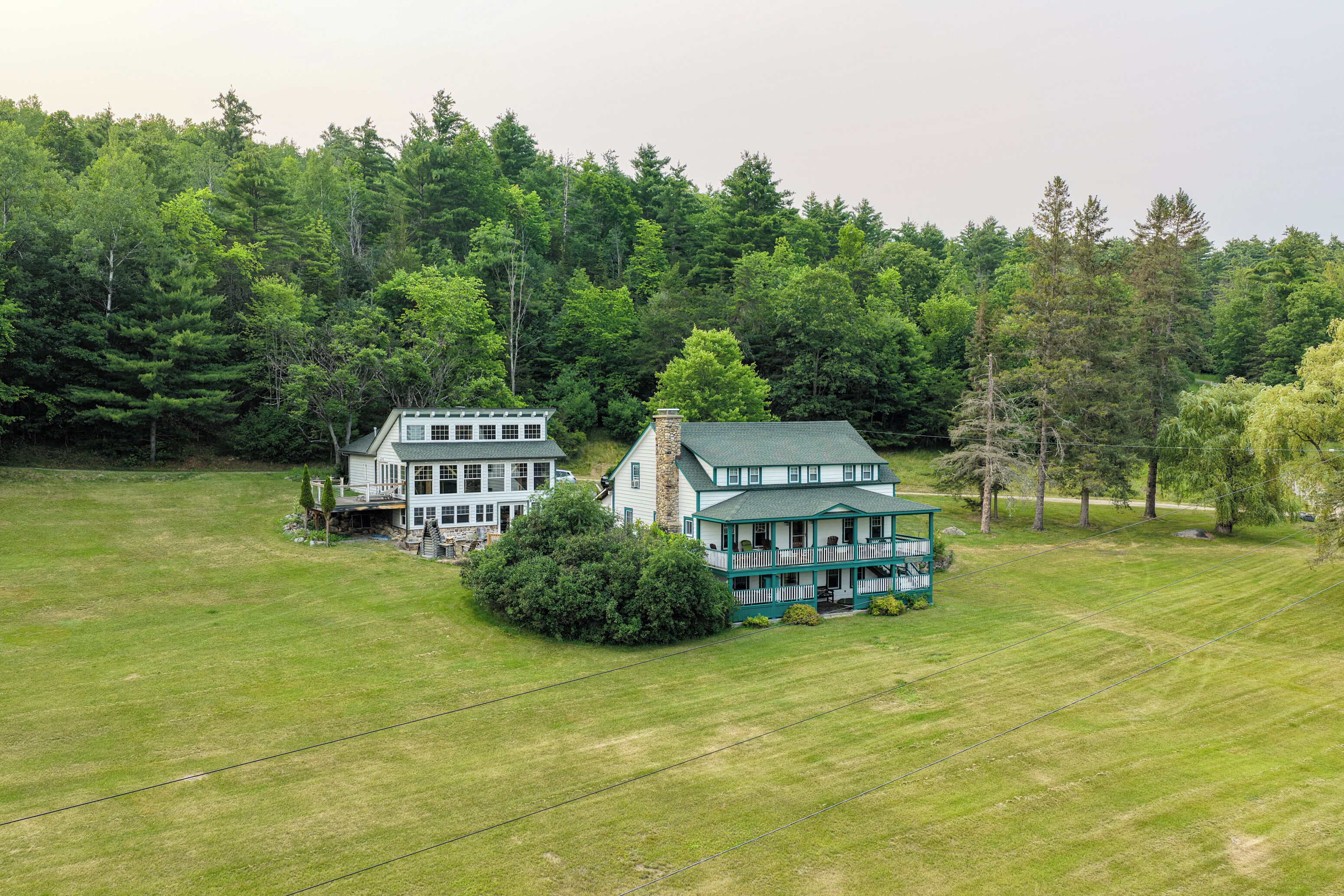Une grande maison à deux étages, dotée d’un toit végétalisé et d’une façade blanche, entourée d’une pelouse bien entretenue et d’une forêt dense.
