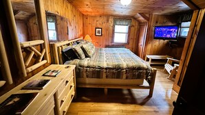 Un dormitorio de cabaña de madera con una cama, un aparador de madera, un televisor y una ventana.