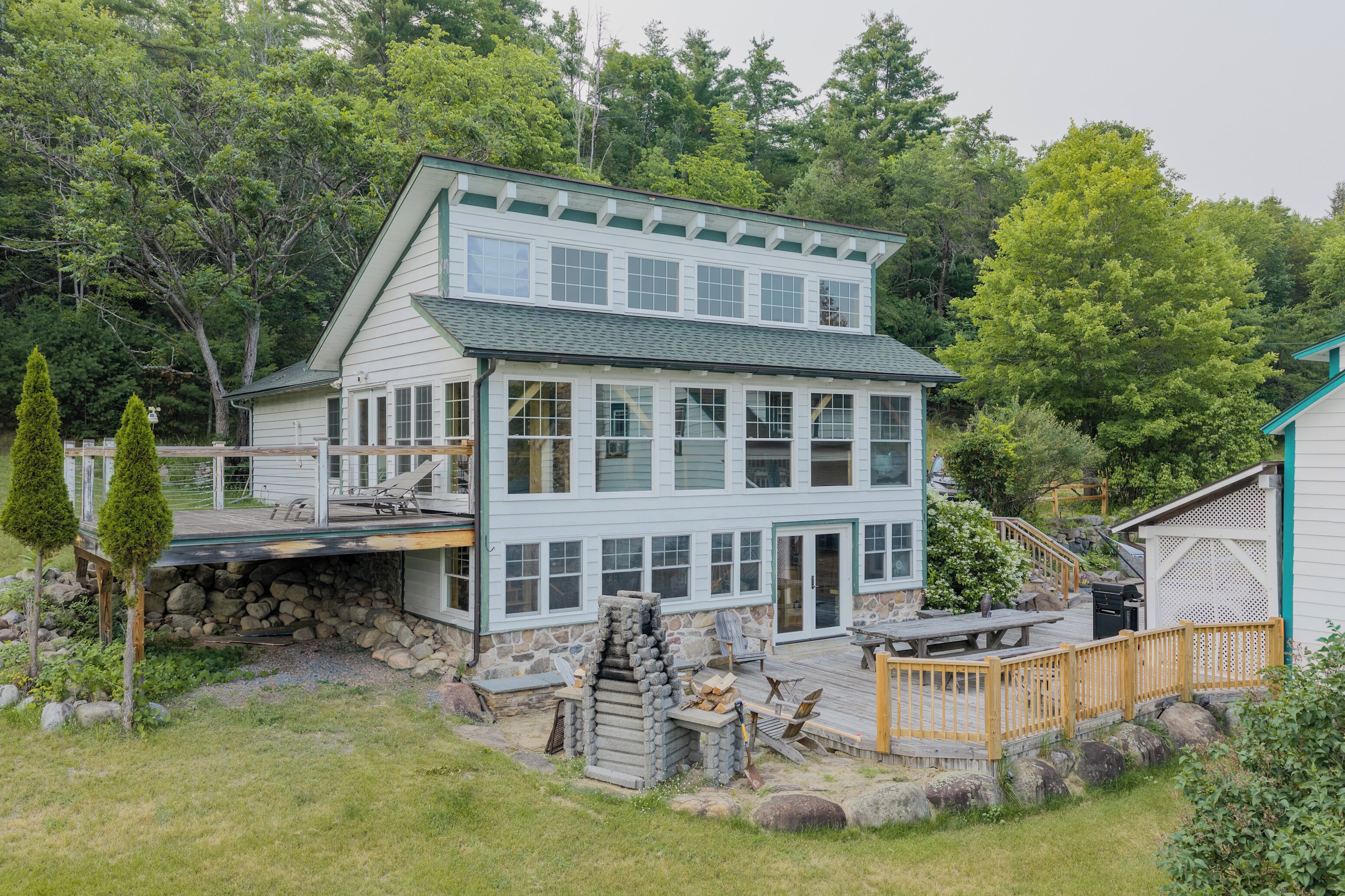 A two-story house with a stone foundation, a deck, and a fenced yard.