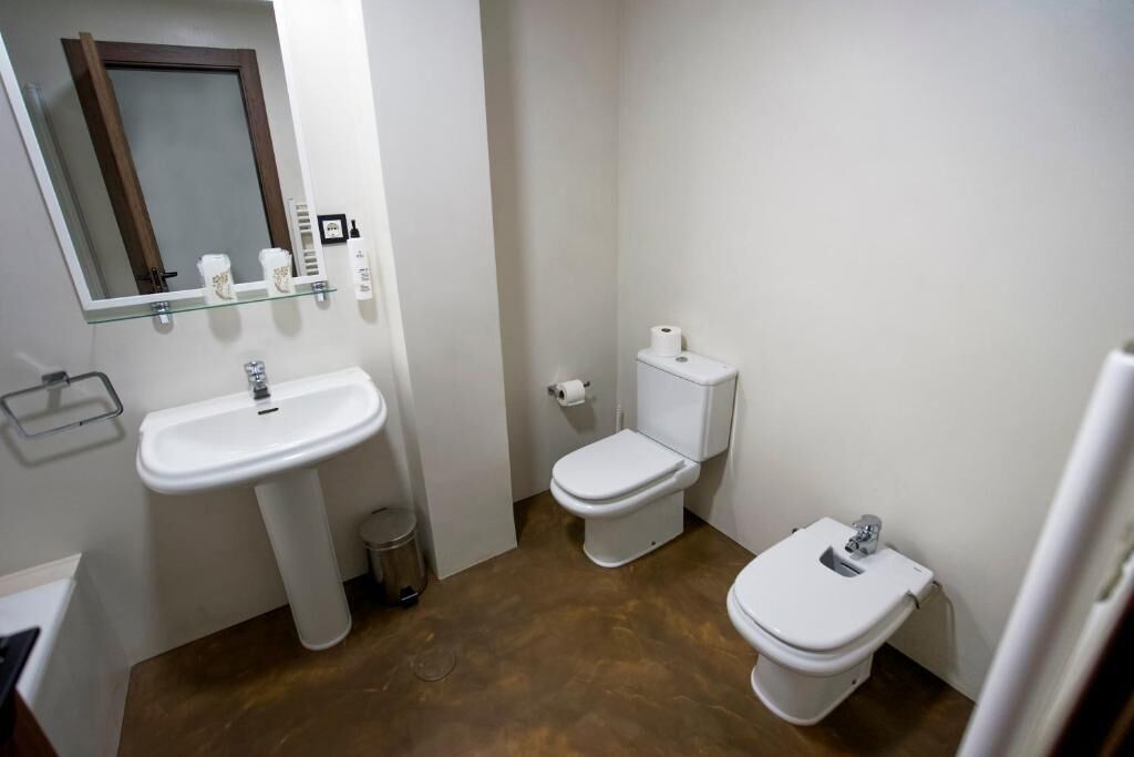 Une petite salle de bain comprenant un lavabo, deux toilettes, un miroir et une étagère en verre où sont rangés les articles de toilette.