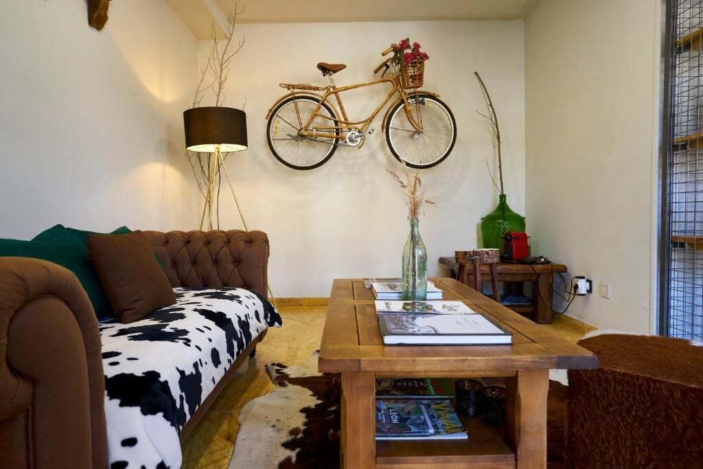 A living room with a sofa, a coffee table, a wall-mounted bicycle, a lamp, and a vase with flowers.