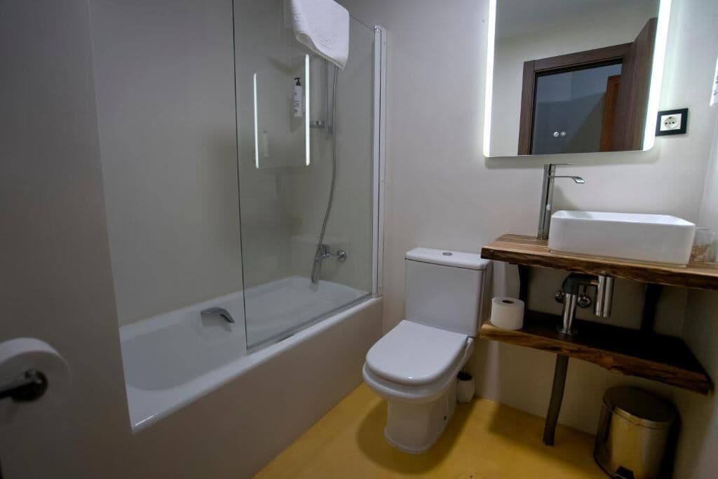 Een badkamer met een douchecabine van glas, een wit toilet en een houten wastafelmeubel met een spiegel.