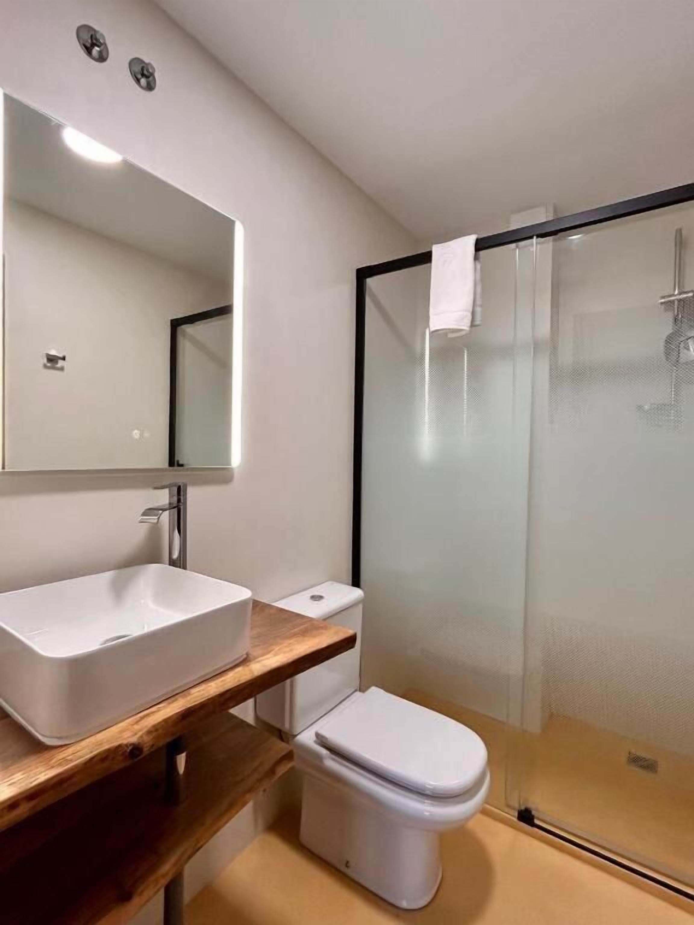 Un baño moderno con lavamanos blanco, inodoro y ducha con mampara de vidrio.