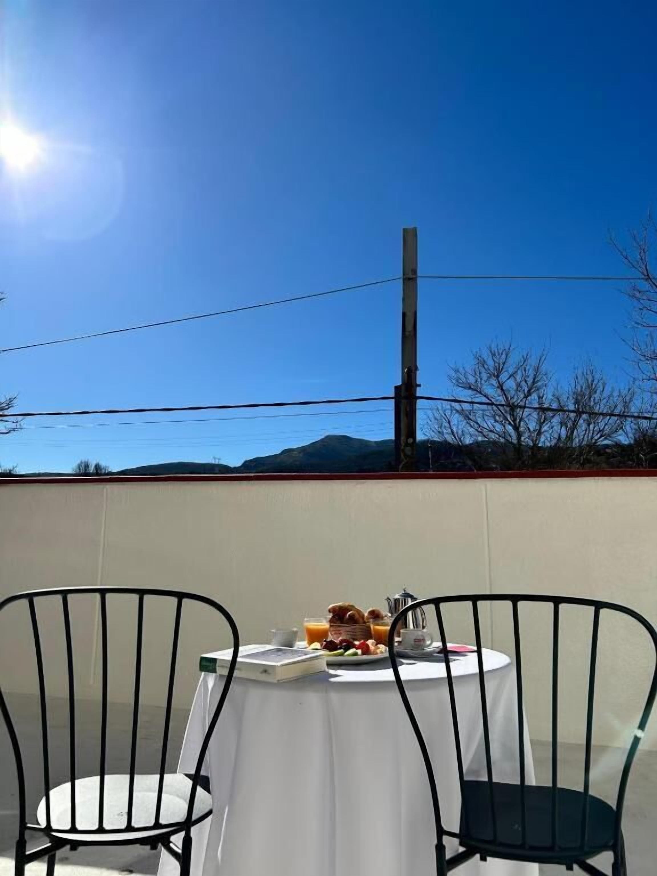 A table with a white tablecloth, two chairs, and a breakfast setting with eggs, bacon, and orange juice.