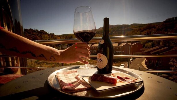 A person holding a wine glass with a bottle of wine on a table with a plate of food. - Hotel Restaurante Bicis & Vacas (La Pola de Gordón)