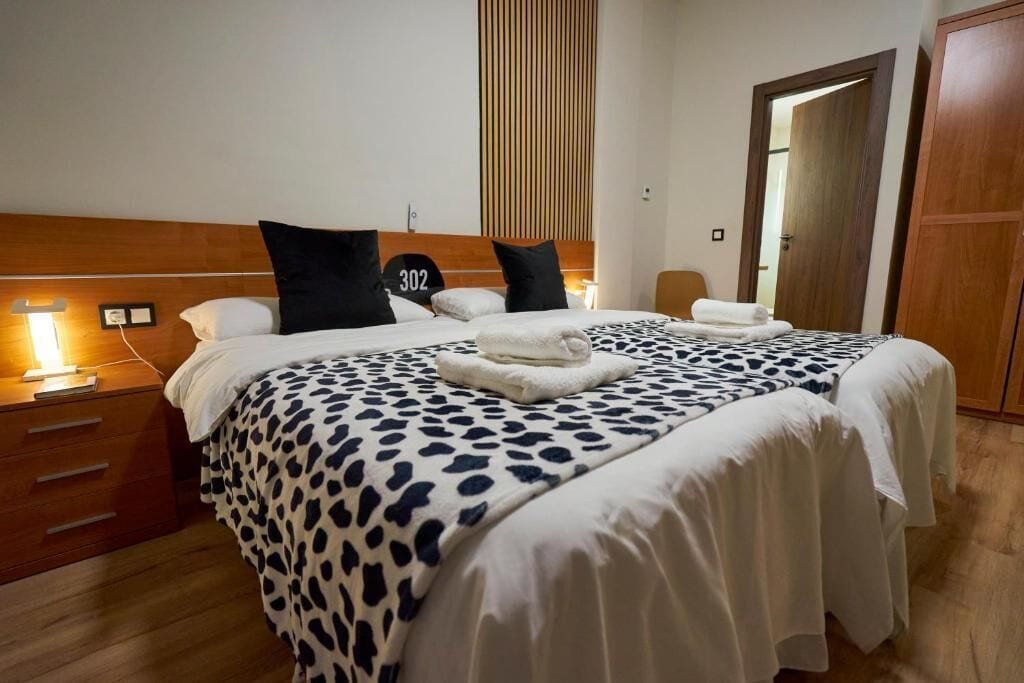 A hotel room with a bed, a wooden headboard, a bedside table, and a door.