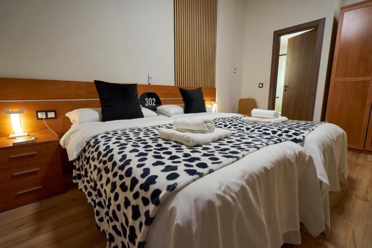 Una habitación de hotel con cama, cabecera de madera, mesita de noche y puerta.