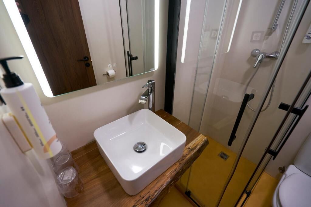 Ein Badezimmer mit einem weißen Waschbecken, einem Spiegel, einer Duschkabine und einer Toilette.