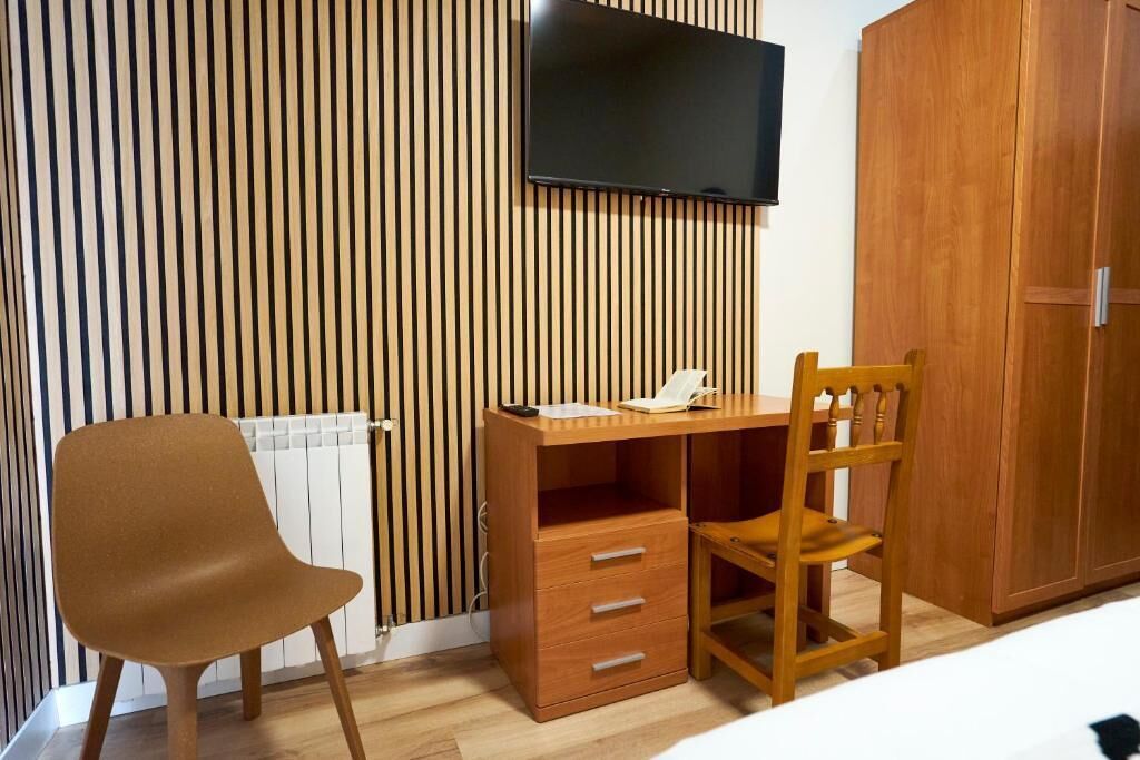 Quarto com escrivaninha de madeira, uma cadeira, guarda-roupa e televisão na parede.