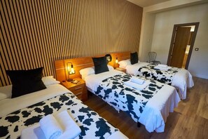 Habitación de hotel con tres camas, cada una con colcha de vaca, cabecero de madera y lámparas de noche.