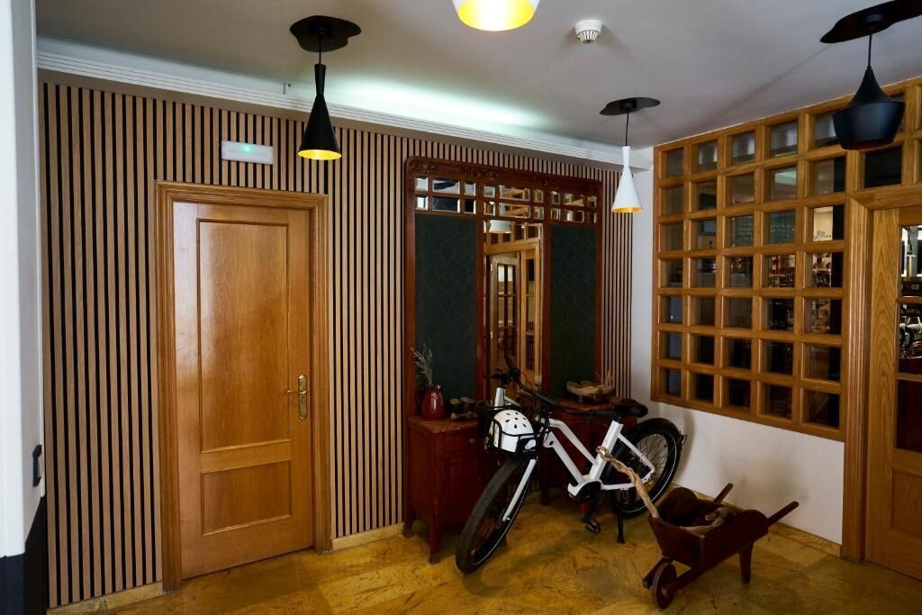 Une pièce avec une porte en bois, un vélo, une petite table sur laquelle est posée une plante en pot et un miroir qui reflète la pièce.