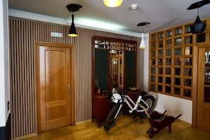 Una habitación con puerta de madera, una bicicleta, una mesita con planta en maceta y un espejo que refleja el interior.