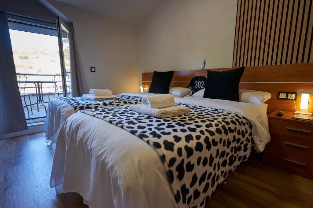 Habitación de hotel con dos camas, un balcón y un cabecero de madera.