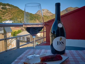 Una mesa con una copa de vino, una botella de vino y un plato de comida en un balcón con vistas a un paisaje montañoso.
