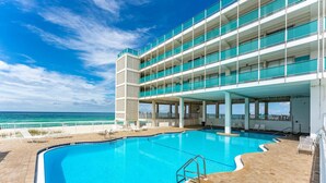 A large outdoor swimming pool with a clear view of the ocean, a multi-level building with balconies, and a covered deck area. - Coastal Vibes - Oceanfront Studio, Resort Pool (Panama City Beach)