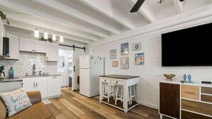 A modern kitchen with white cabinetry, a wooden dining table, and a large TV mounted on the wall. - Coastal Vibes - Oceanfront Studio, Resort Pool (Panama City Beach)