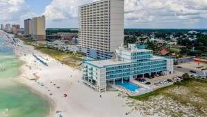 A beachfront hotel with multiple floors, a swimming pool, and a parking area. - Coastal Vibes - Oceanfront Studio, Resort Pool (Panama City Beach)