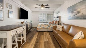 A cozy room with a bed, a wooden desk, a television, and a ceiling fan. - Coastal Vibes - Oceanfront Studio, Resort Pool (Panama City Beach)
