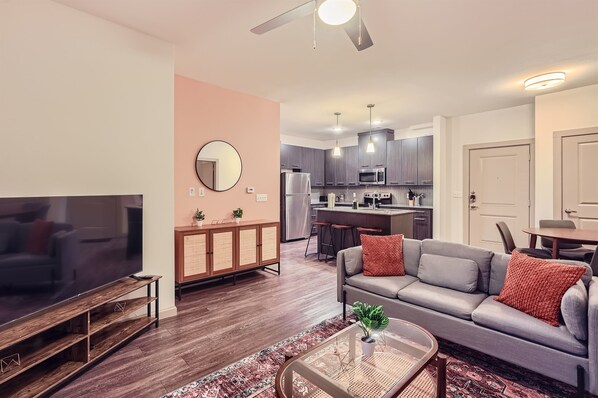 A modern living room with a flat-screen TV, a gray sofa with red cushions, a coffee table, and a patterned rug. - Serene 3B Getaway | Pool, Gym, Parking, Pet Wash (Leander)