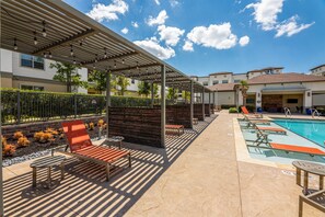 A covered outdoor area with a pool, lounge chairs, and a pergola with string lights. - Serene 3B Getaway | Pool, Gym, Parking, Pet Wash (Leander)
